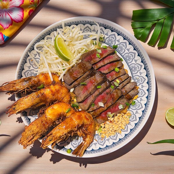 Sliced steak, large prawns, bean sprouts, peanuts, and lime on a decorative plate.