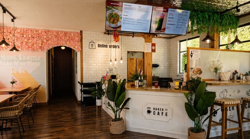 Interior of Baker St Cafe with a white counter, menu screens, and a pink floral wall.