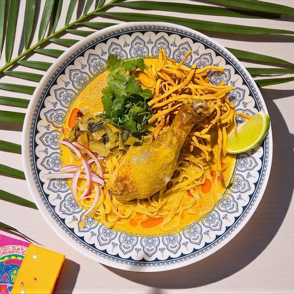 Chicken Khao Soi with curry noodles, crispy noodles, cilantro, red onion, and lime.