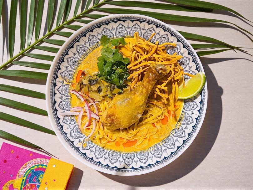 Chicken Khao Soi with curry noodles, crispy noodles, cilantro, red onion, and lime.