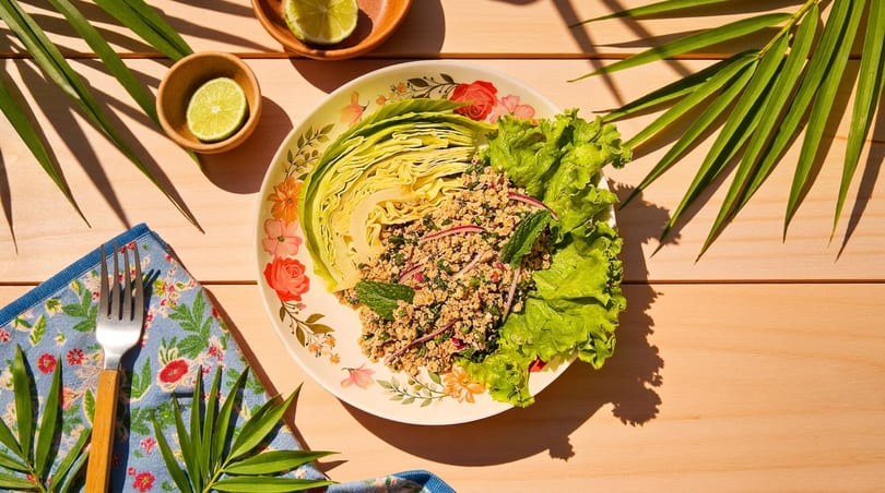 Larb Gai, a Thai minced chicken salad, served with cabbage, lettuce, and lime on a wooden table.