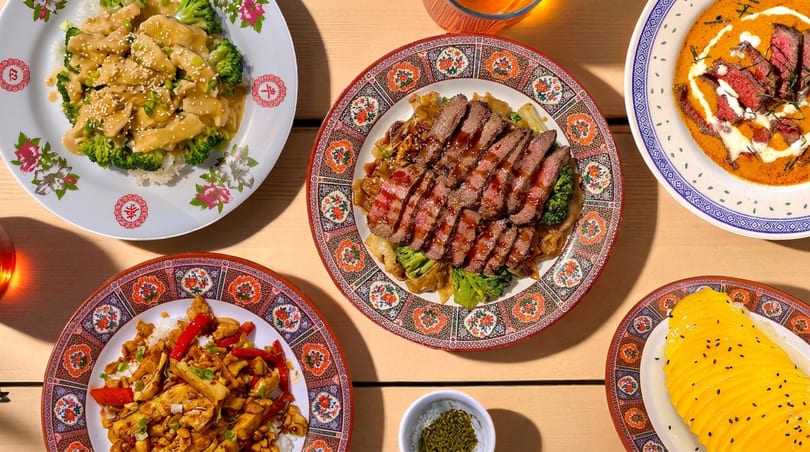 An overhead shot of five colorful plates of Asian cuisine, including beef, chicken, and mango sticky rice.