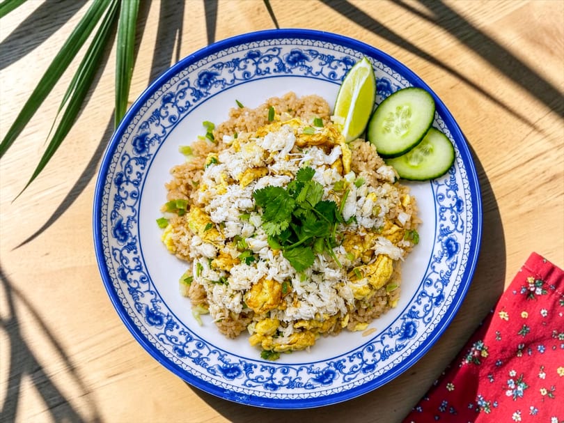 Crab fried rice with scrambled egg, cilantro, lime, and cucumber on a patterned plate.